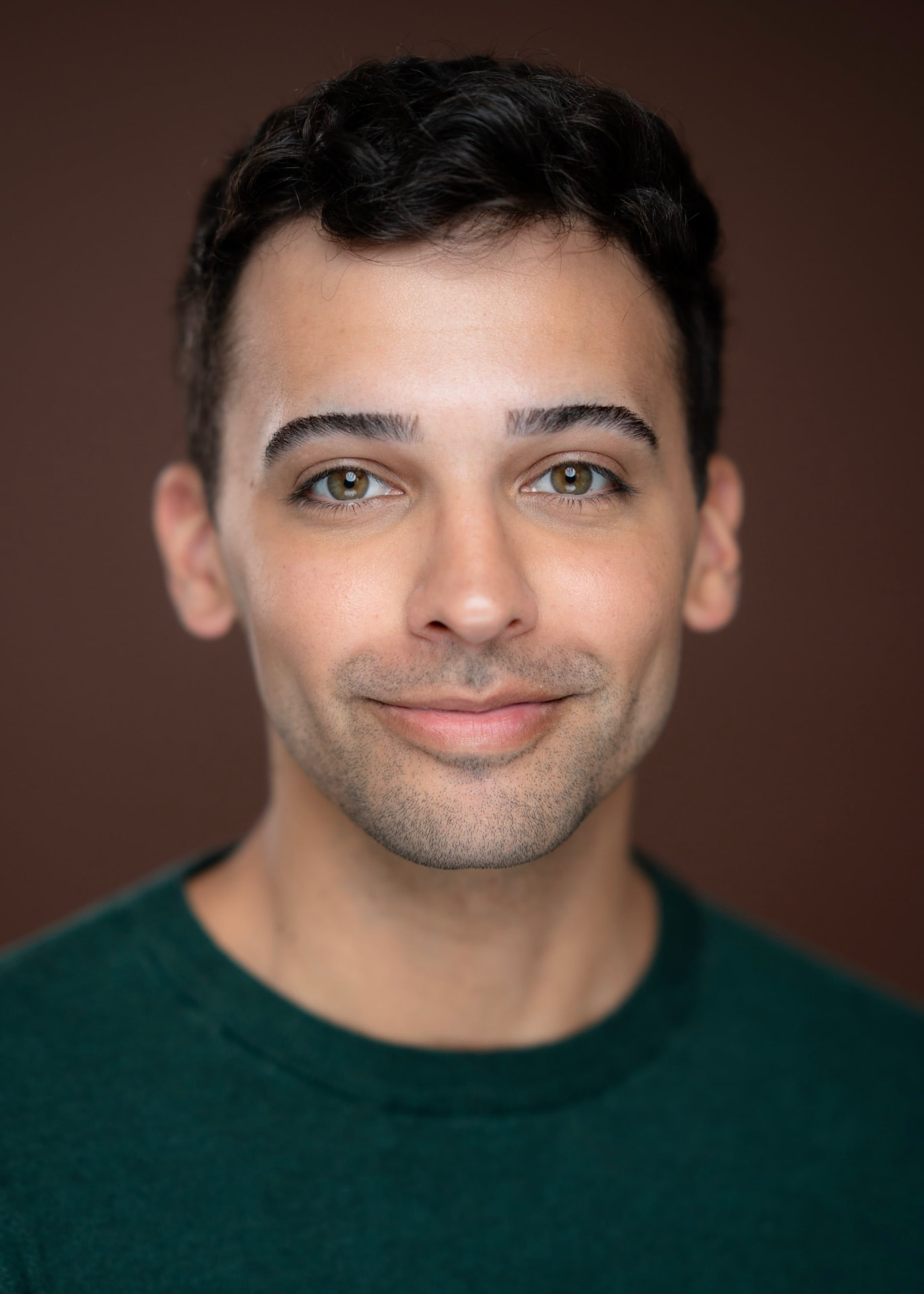 Headshot in a green sweater against a warm brown backdrop